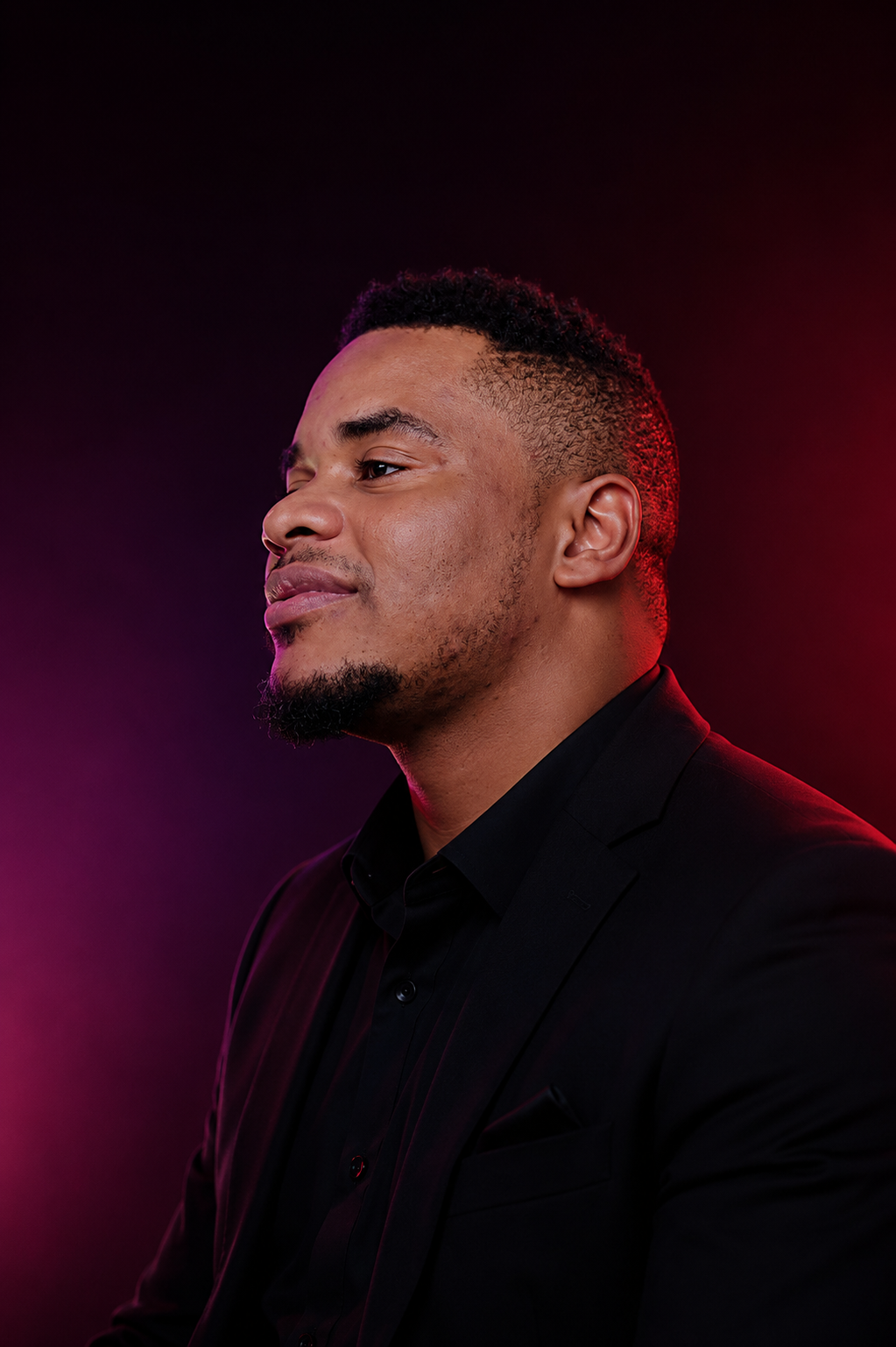 Gabriel Emmanuel Idachaba in a black suit, photographed in profile against a red and purple studio background